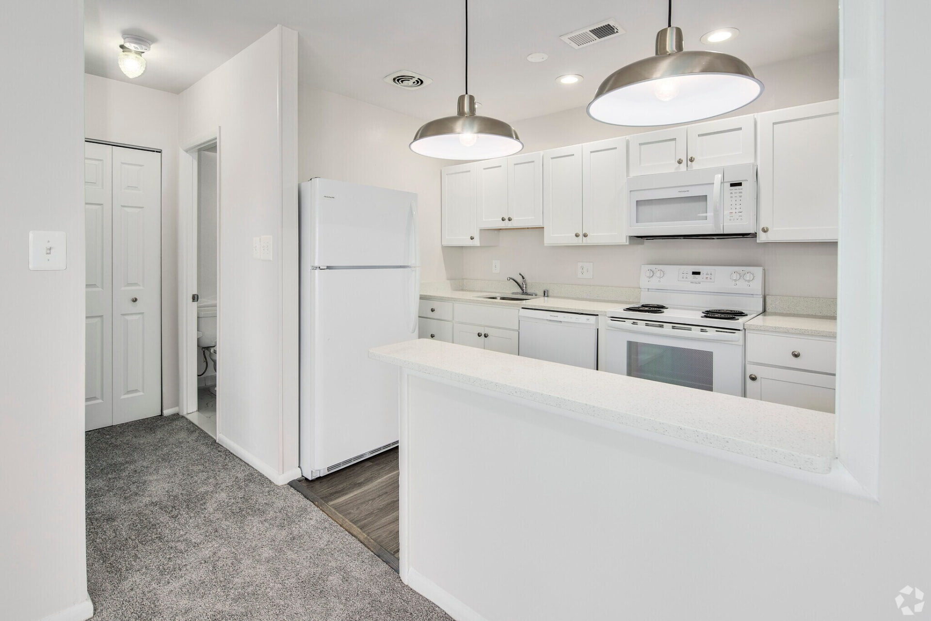 Renovated apartment kitchen with white cabinets, white appliances and pendant lights